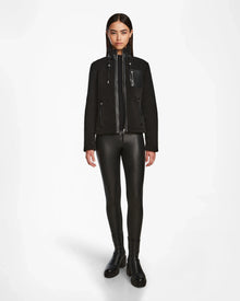 A woman faces forward wearing the Rudsak MILANA - 8524604 Black jacket, featuring vegan leather details, paired with black faux leather leggings and ankle boots against a plain white background.