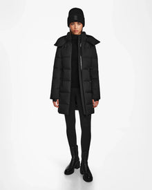A person faces forward wearing the Rudsak MIRIAM - L122523 BLACK womens down puffer coat, paired with a black knit beanie, black pants, and black boots against a plain white background.
