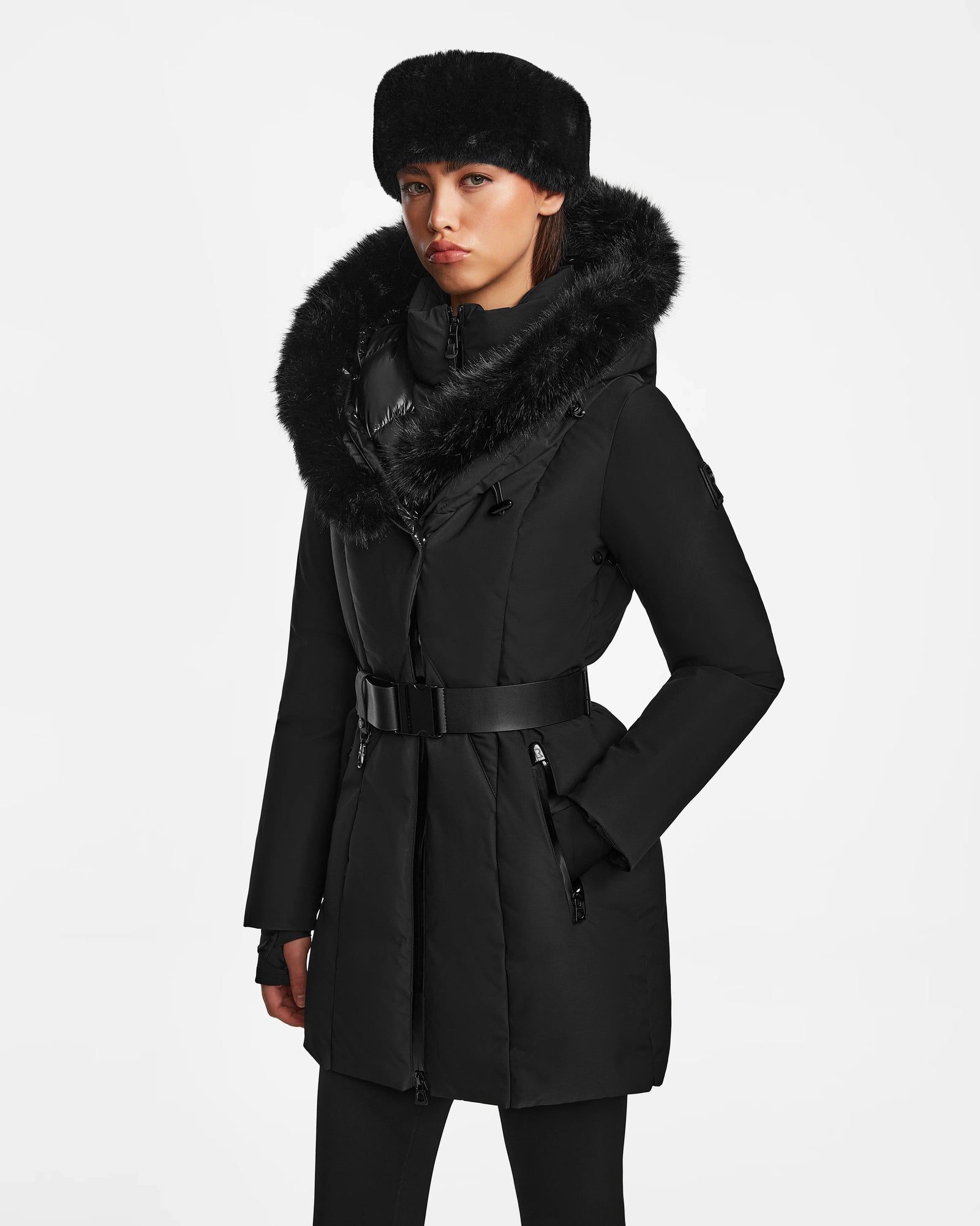 A woman wearing the Rudsak MODA M - 8124555 Black fur-trimmed winter coat and matching black leggings stands against a plain white background, looking directly at the camera with a neutral expression.
