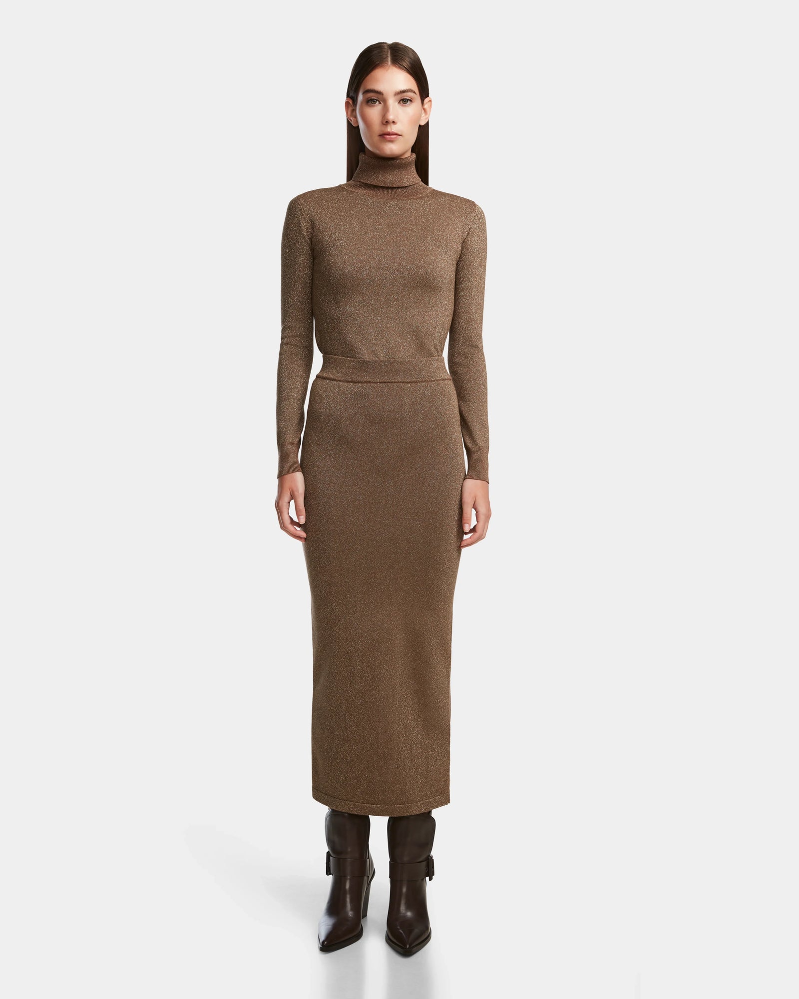 A woman faces forward against a plain white background, wearing the Rudsak MONICA - 8524516 Antique Bronze long, body-hugging turtleneck dress with long sleeves and dark brown heeled boots.