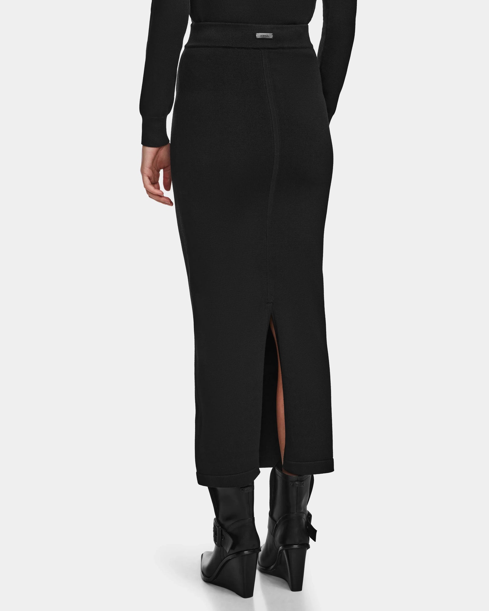 Wearing the Rudsak MONICA - 8524516 Black skirt, styled with black ankle boots, a person is shown from behind against a plain background.