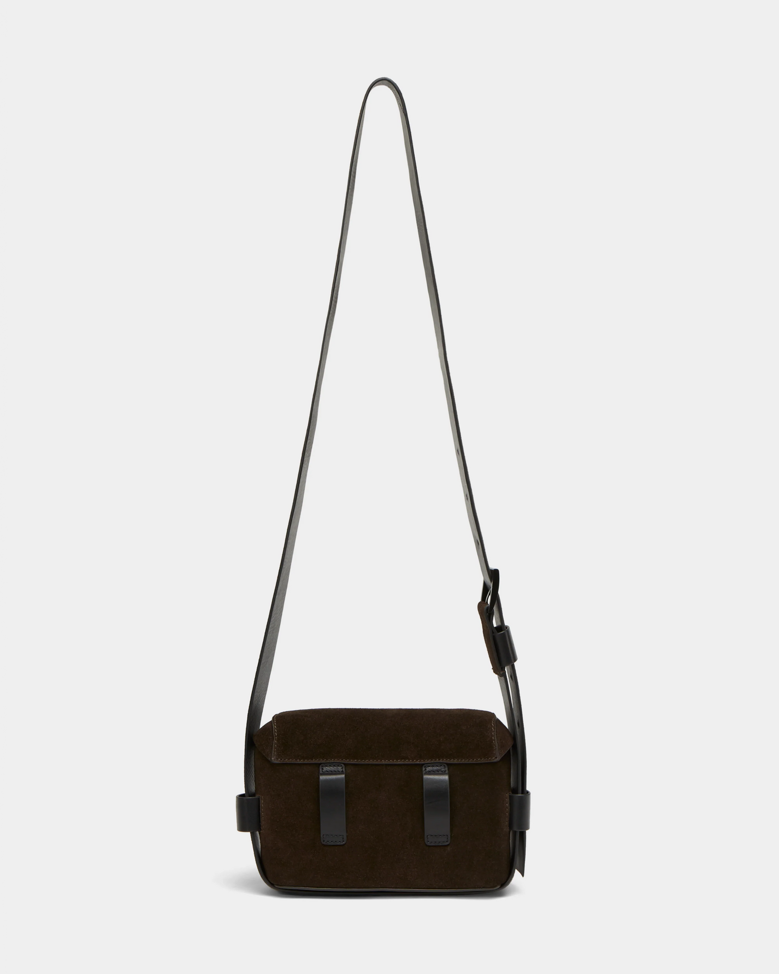 The OFILIA S - 8324521 Espresso by Rudsak is a small, rectangular dark brown suede crossbody bag with a long adjustable leather strap and two black leather accents on the front, shown against a plain light background.