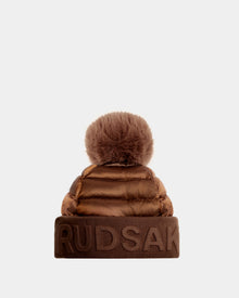 Rudsaks OLYA - 8422504 in Antique Bronze is a womens brown puffer winter hat with a wide cuff embossed with RUDSAK and topped with a large, fluffy fur pompom.