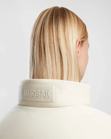 A person with straight, blonde hair is seen from behind, wearing the Rudsak OPRAH - 8124708 Iceland textured white women’s cropped down puffer with a raised collar featuring the embossed brand name.