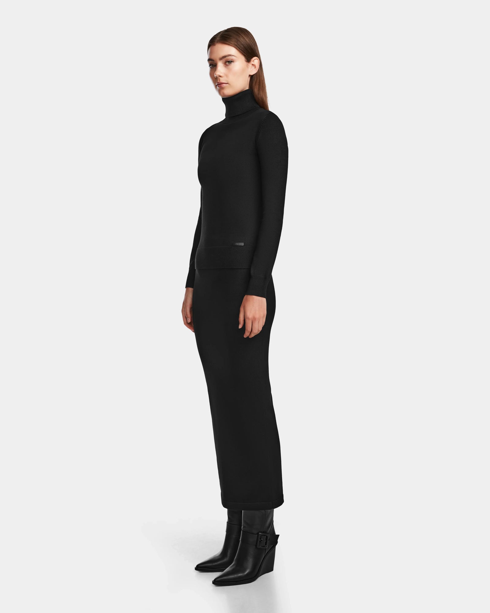 A woman wears the RALDI - 8524605 Black by Rudsak, a womens knit turtleneck dress with subtle metallic thread detailing.