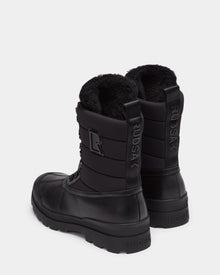 The Rudsak REAGAN - 6224501 Black men’s winter boots feature thick soles, lace-up fronts, soft furry linings, a back pull tab, and the Rudsak name embossed vertically for a stylish finish.