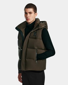 A young man stands facing forward with a neutral expression, wearing the Rudsak REN M - 9123512 Army M weather-resistant dark olive green puffer vest over a black turtleneck against a plain light background.