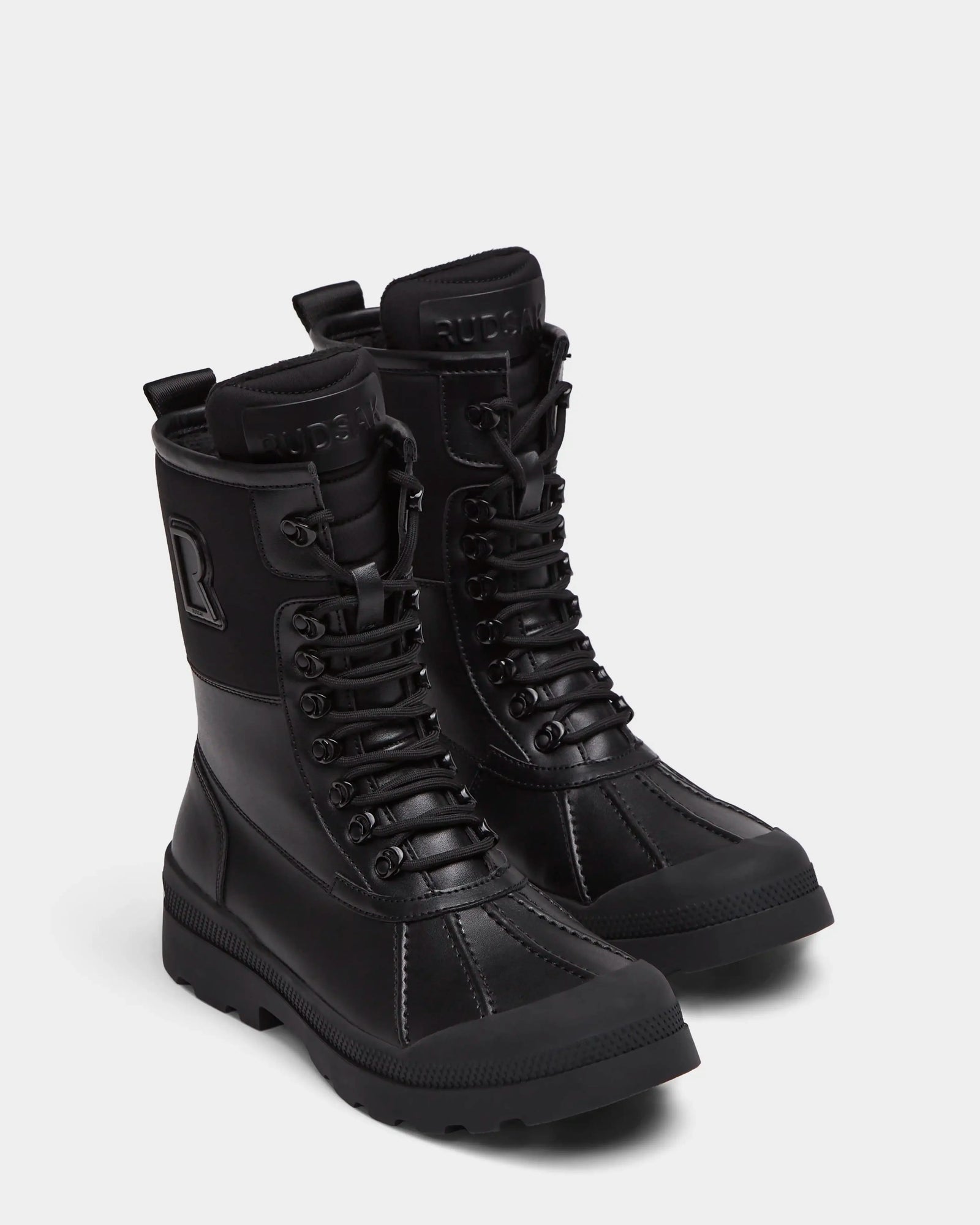The Rudsak RITA - L222502 Black women's winter boots feature mid-calf lace-up design, weather-treated leather, rugged soles, and embossed branding on the tongue and side, shown on a plain light background.