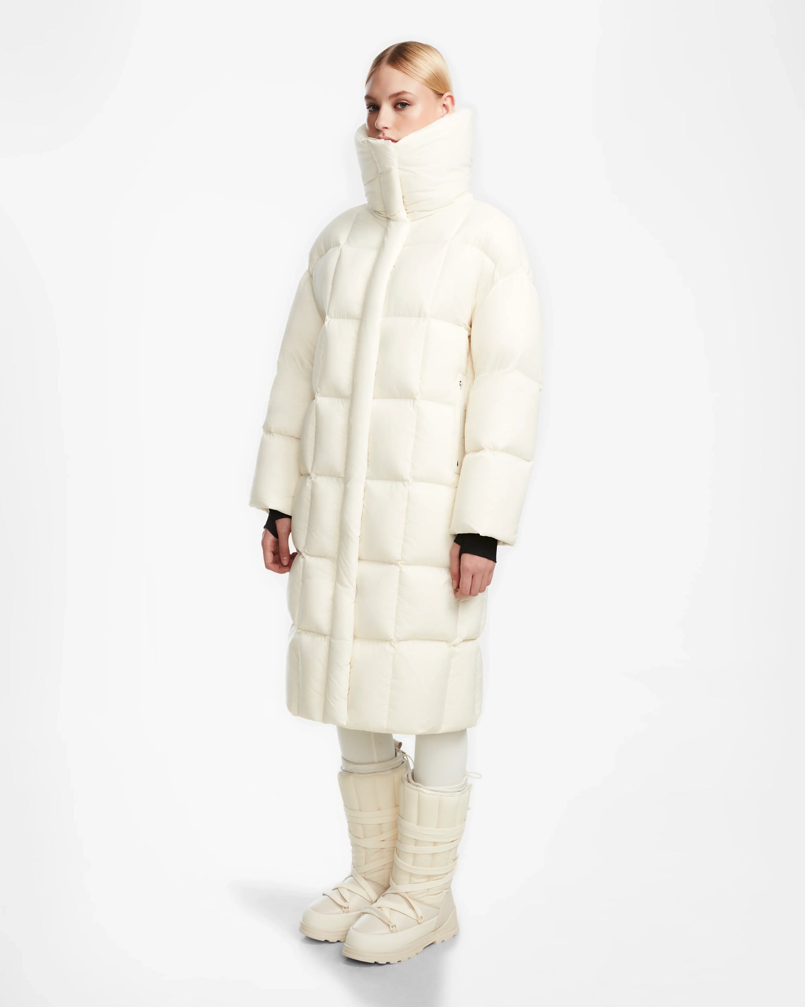 A person wears the Rudsak SASH - 8124536 Iceland women’s long down puffer coat with RDS-certified down, matching pants, and padded winter boots, standing against a plain white background.
