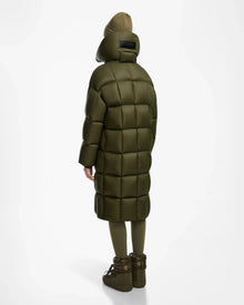 A person stands facing away, wearing the Rudsak SASH - 8124536 Loden Green women’s long down puffer coat with RDS-certified down, paired with matching leggings, chunky boots, and a brown knit beanie against a white background.