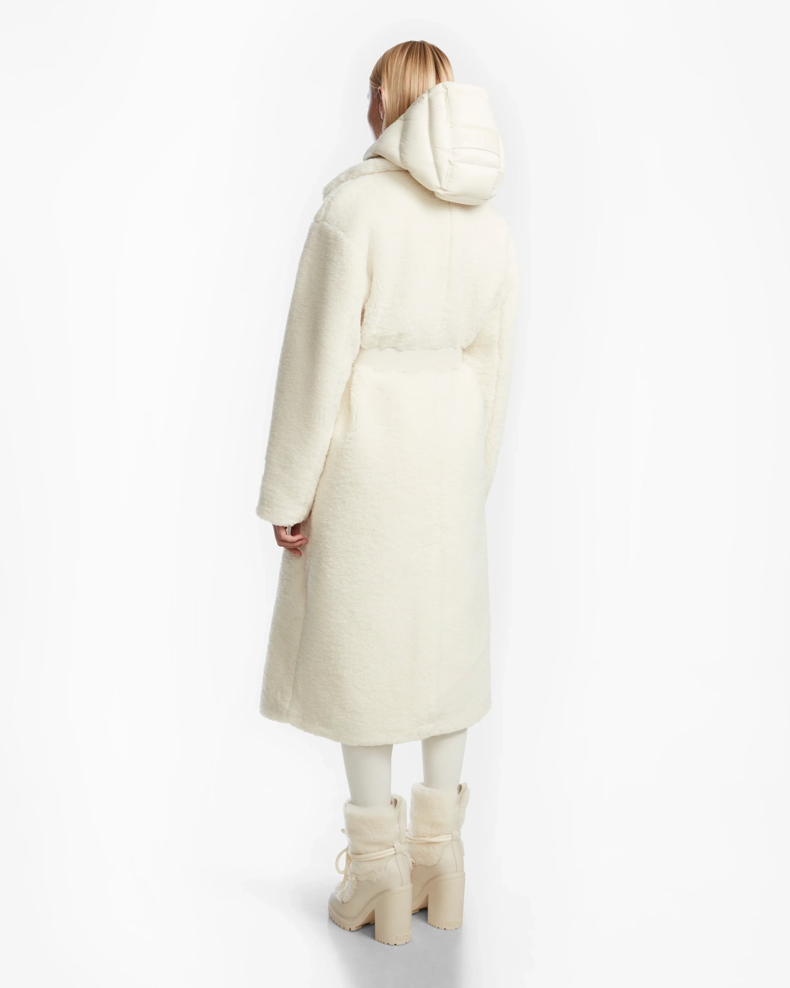 A person with light hair faces away, wearing Rudsaks TINA - 8123578 Iceland ivory textured womens trench coat with a removable hooded bib, matching pants, and chunky off-white boots against a plain white background.