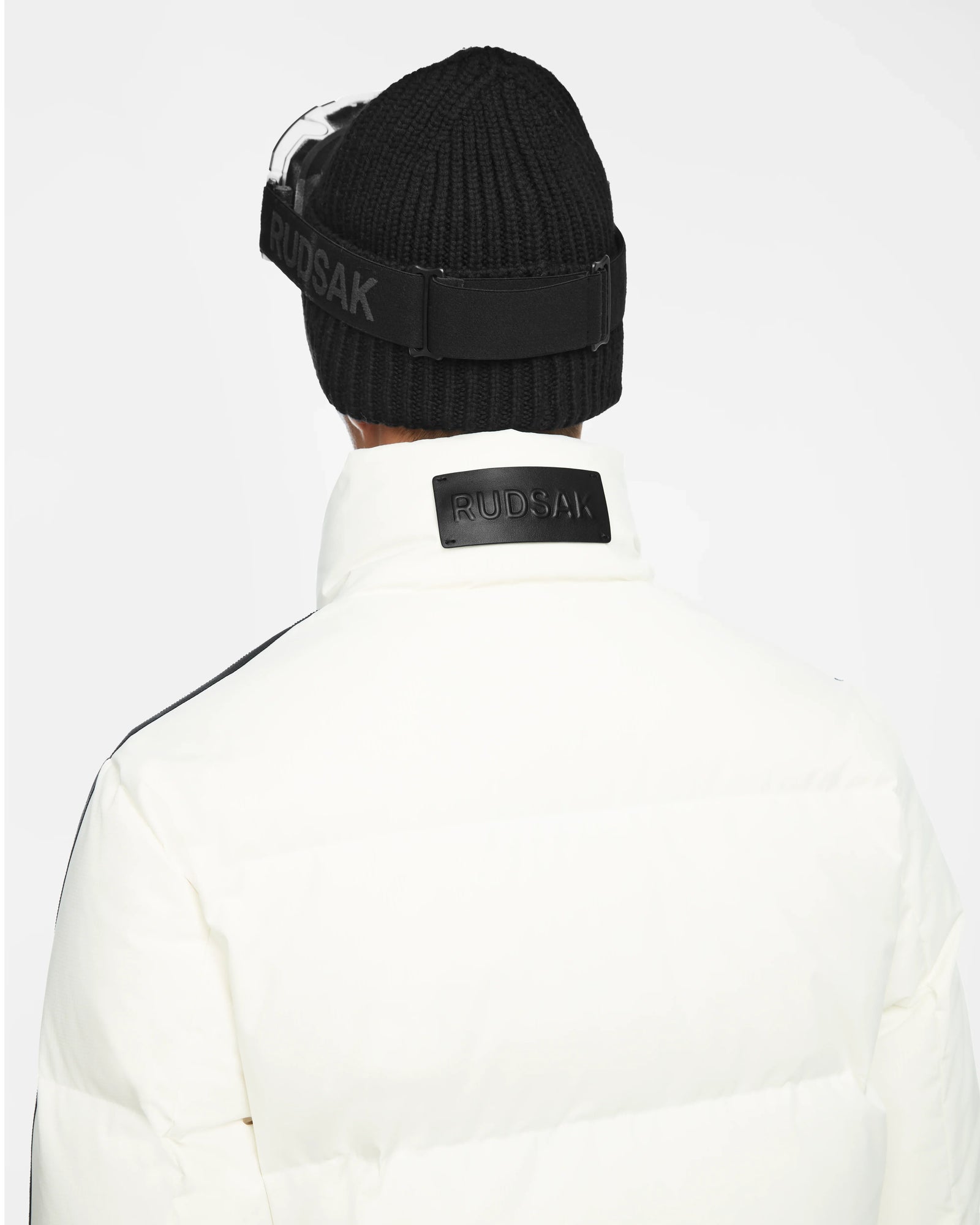 A person is shown from behind wearing a black knit beanie and the Rudsak USHER - 6124516 Optic White winter ski jacket with high collar, featuring RDS-certified down insulation, against a plain white background.