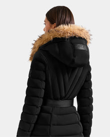A person with straight brown hair is seen from behind wearing the Rudsak ALISA L - L125574 Black quilted puffer coat with a wide faux-fur trim hood and belt, set against a plain light background.