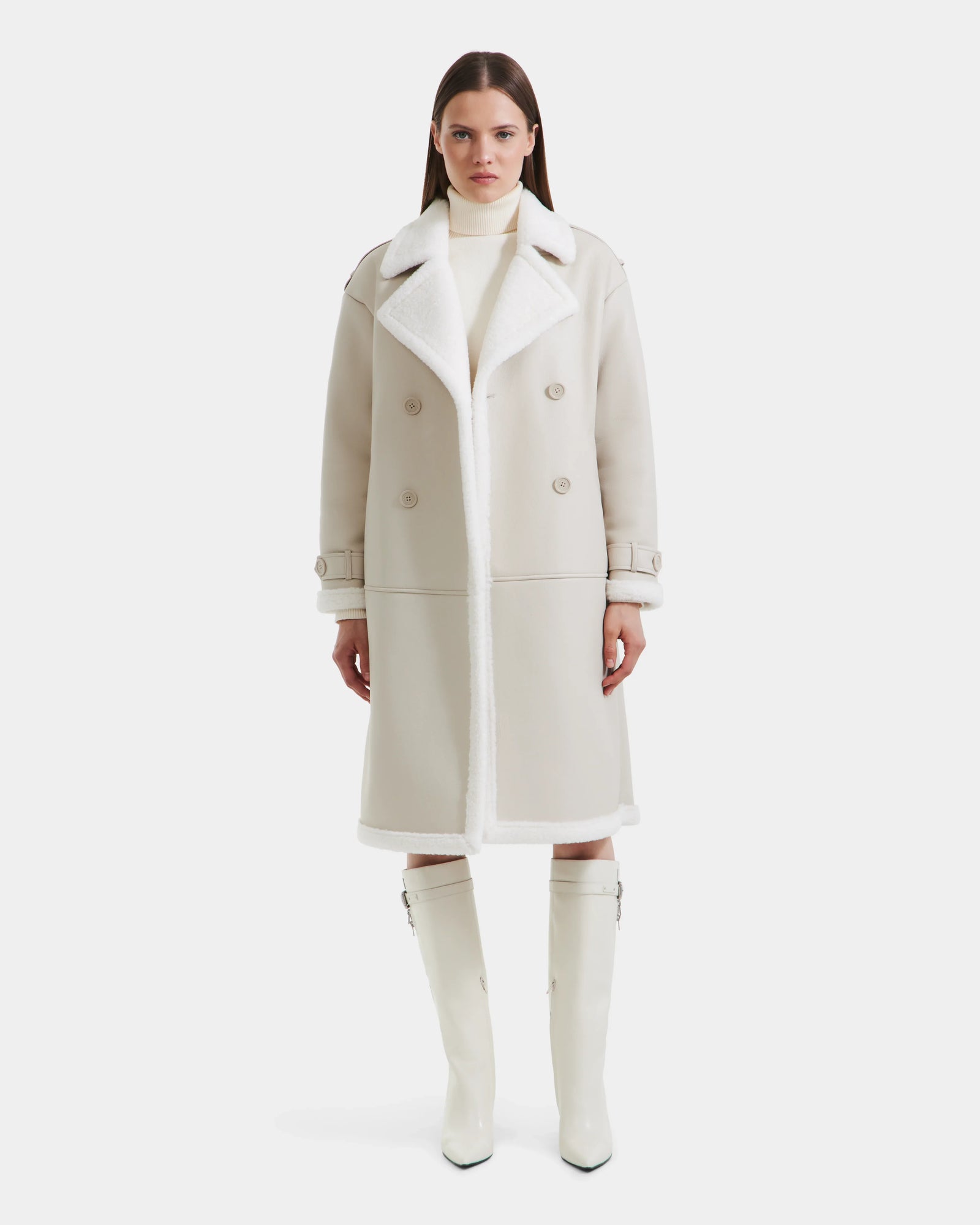 A woman faces forward in a Rudsak DARCY - L125539 Vanilla women's winter coat—a long cream faux sherpa teddy with a wide white collar—paired with a white turtleneck and knee-high boots, set against a plain white background.