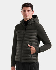 A man stands facing forward with one hand in his pocket, wearing the Rudsak DURIN M - M125530 Dark Olive men’s hooded jacket, featuring quilted front panels and waterproof zippers, against a plain light background.