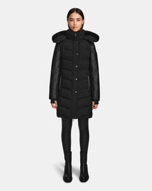 A woman faces forward against a white background, wearing the Rudsak ELSA - L123535 Black quilted down puffer winter coat with a hood, paired with black leggings and boots.
