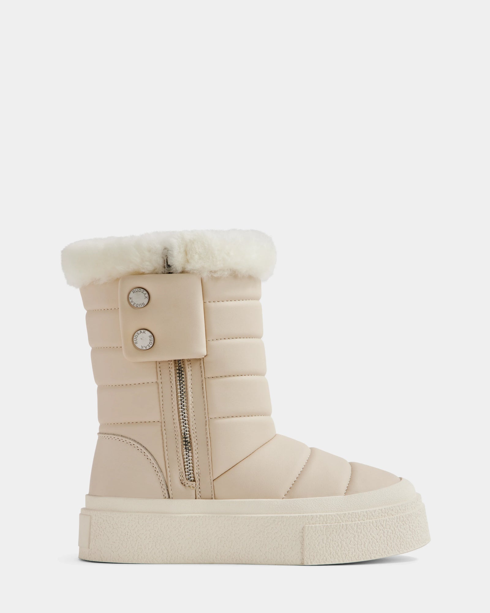 The KATHIE - L225516 Vanilla by Rudsak is a beige quilted women’s mid boot with a thick white sole, faux fur trim, side zipper, and two decorative buttons on a strap near the opening. Shown on a plain white background.