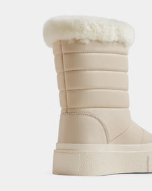 A close-up of the Rudsak KATHIE - L225516 Vanilla women's mid boot, featuring quilted beige vegan leather, a thick textured sole, and a fluffy white faux fur cuff, displayed against a plain white background.