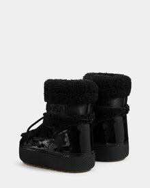 The Rudsak KATHY Y - 1224500 Black boots feature water-repellent shiny patent leather, textured cuffs, and lace-up details, shown from the back on a light gray background.