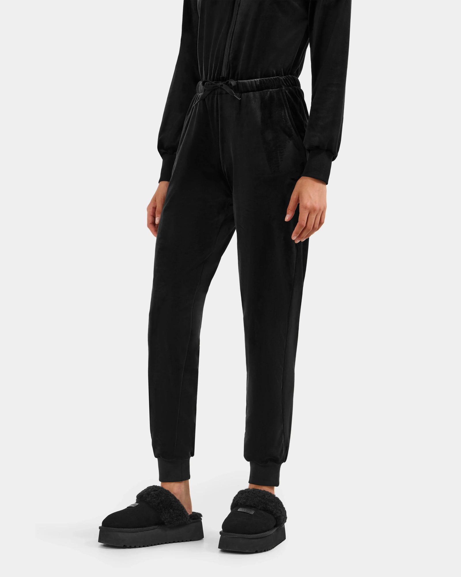 Wearing Rudsak's KETZY - L525503 Black jogger pants and black fuzzy slippers, a person stands against a white background with their women's velour hooded jumper partially out of frame.