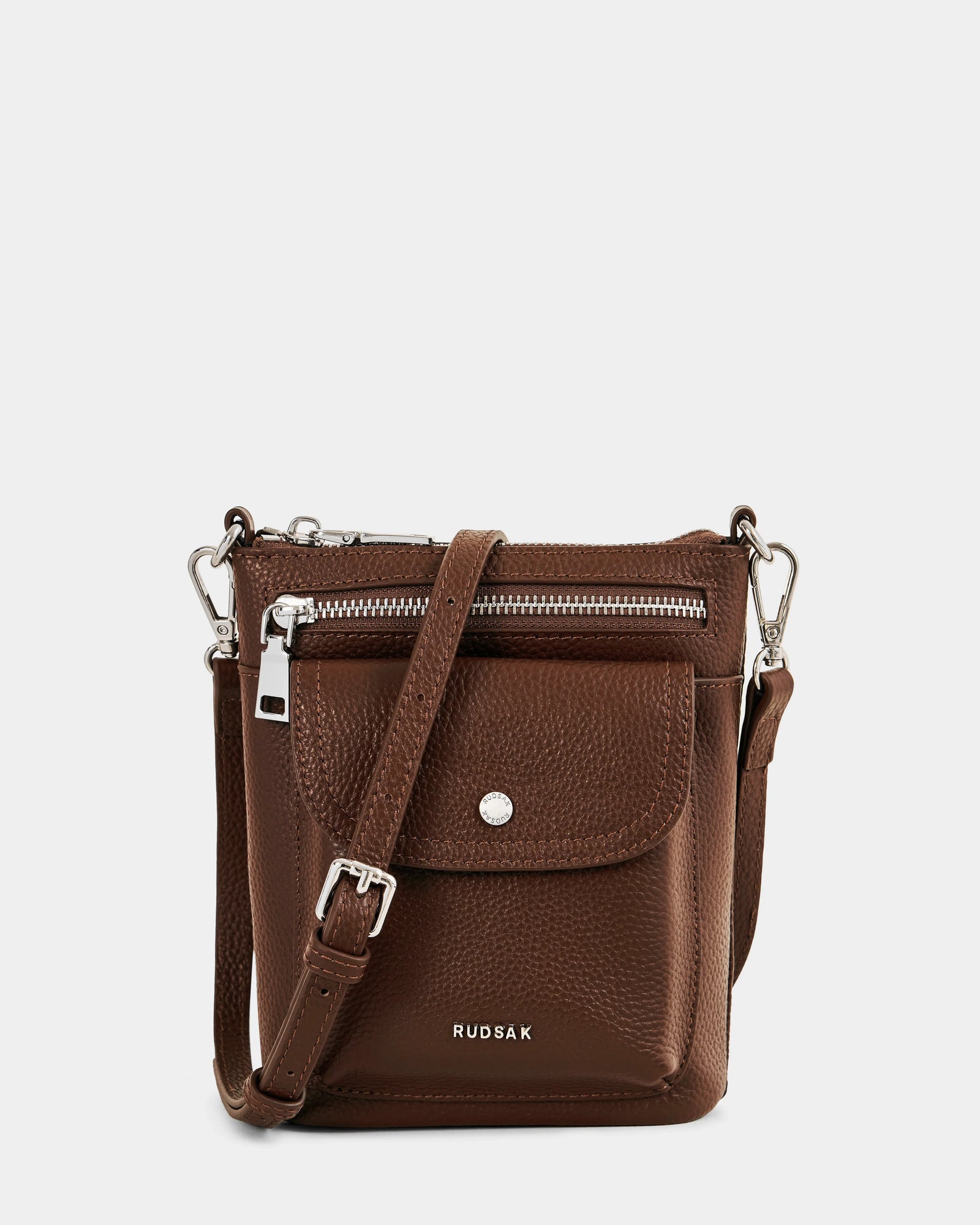 The LILA - L325513 Mocha by Rudsak is a compact brown pebbled leather crossbody bag with a front zip pocket, flap pocket with snap button, and adjustable strap. "RUDSAK" is printed in white—ideal for city-ready daily style.