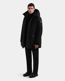 A man faces forward against a light background, wearing the Rudsak MITCHELL - M125513 Black RDS-certified down winter parka, paired with black pants, shoes, and top. His arms rest relaxed at his sides.
