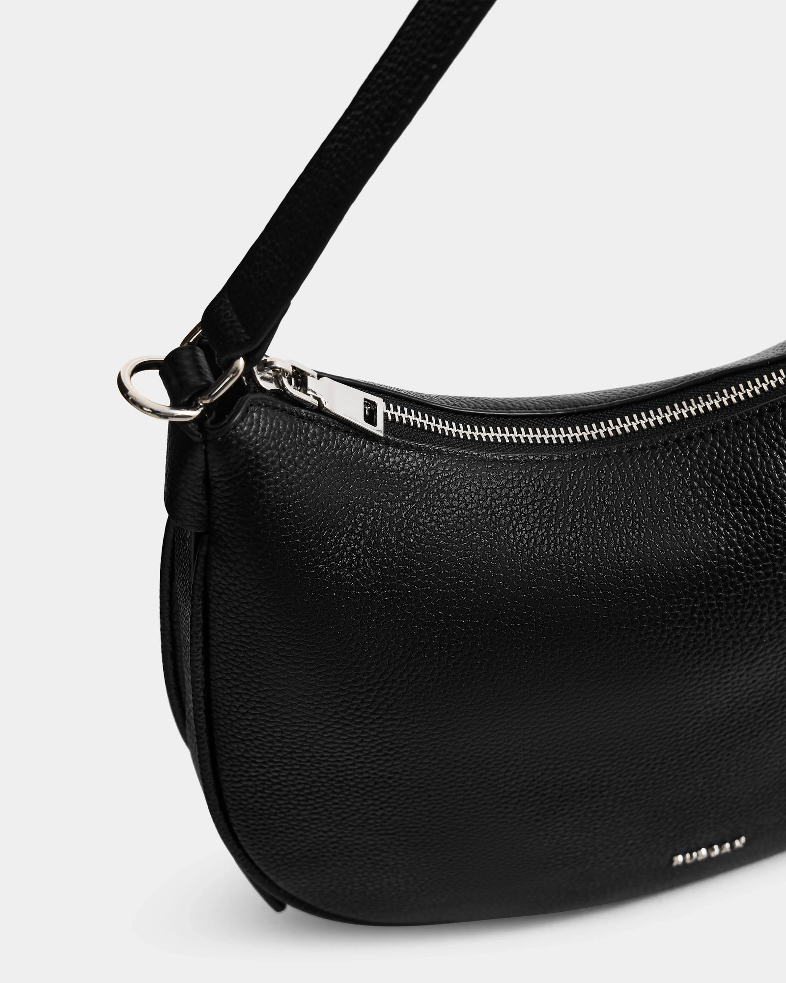 Close-up of the Rudsak SYLVIA - L325515 Black crossbody bag, crafted in pebbled leather with a silver zipper, small metallic logo, shoulder strap, and crescent silhouette.