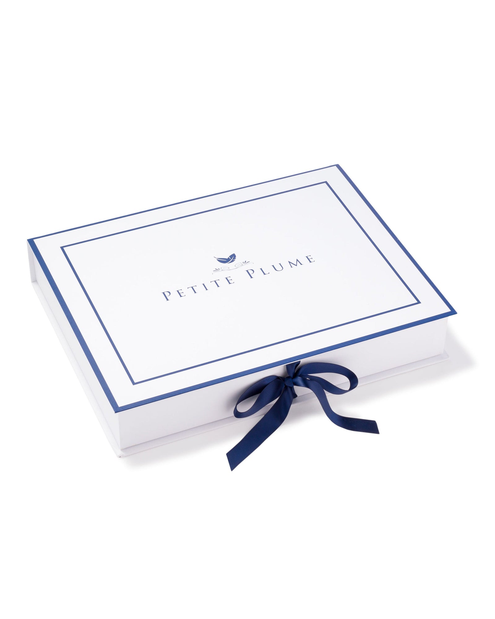 A rectangular box, featuring PETITE PLUME on the lid with a bird logo above, exudes luxury with its white and blue design and side bow. It encloses the Mens Silk Pajama Set in Black by Petite Plume, highlighting its machine-washable silk charm.