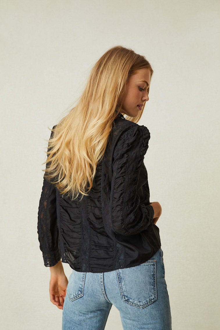 Back image of model wearing black long sleeve blouse with button up front, lace panels and puff shoulders.