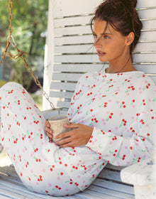 Woman wearing a matching white pajama set with a red cherry print, featuring a long-sleeve top and wide-leg pants