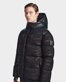 A man wears the Rudsak RONNY M - M123512 Camo Black hooded down puffer, showcasing sleek and weather-resistant men’s outerwear.