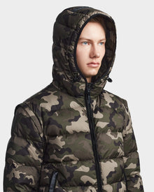 A young person in a Rudsak DEMIAN M-R - M123504 Camouflage mens down puffer, made from sustainable recycled fabric, looks to the side against a plain light background.