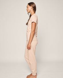 A woman stands sideways, facing left in Petite Plumes Womens Pima Lounge Pants in camel and a matching beige T-shirt. She is barefoot on a plain white background, with straight hair cascading down her back.