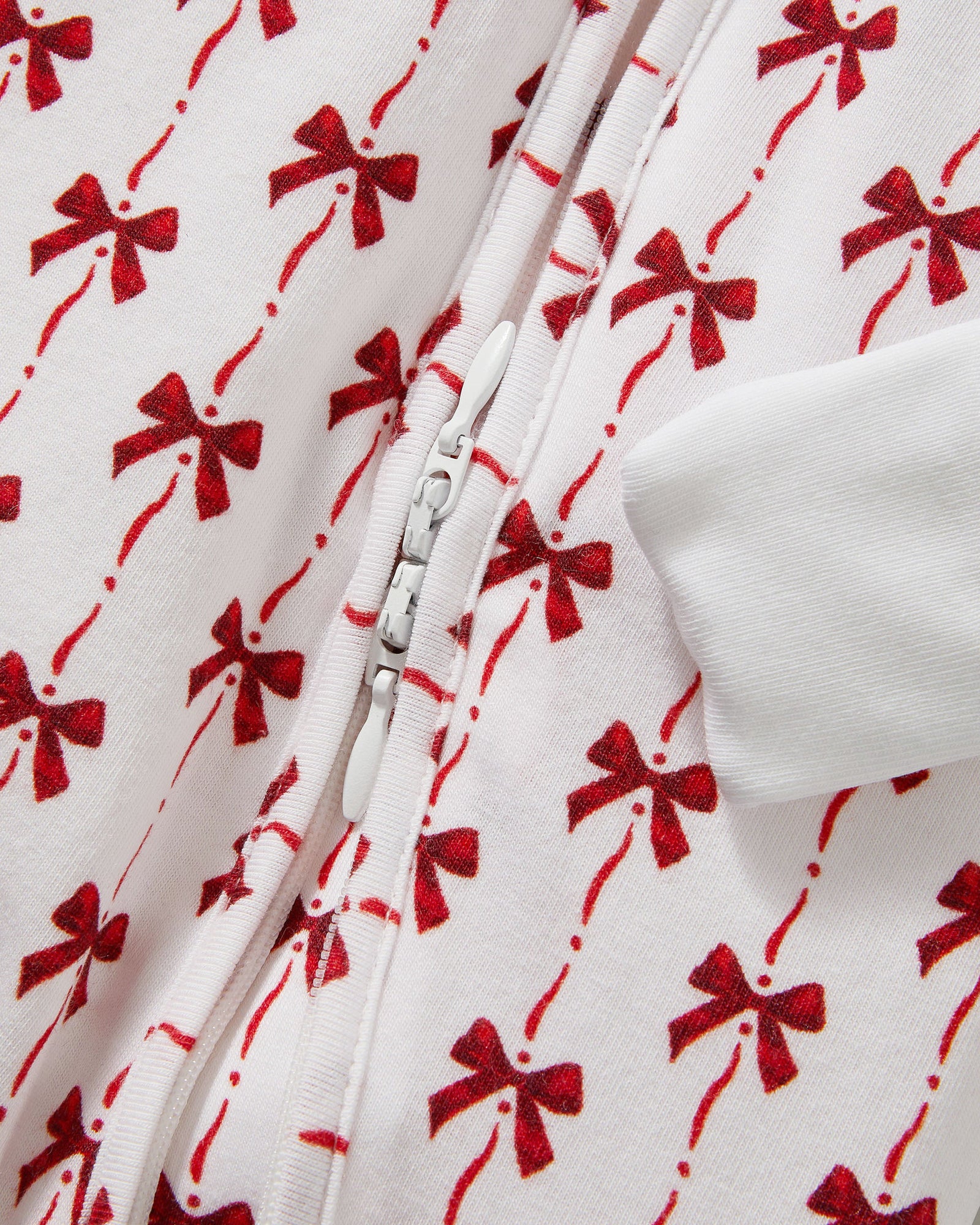The Baby's Pima Peekaboo Romper in Blissful Bows is a white long-sleeve onesie with cuffs, adorned with festive red bows and a convenient back zipper.