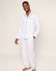 A person smiles in Petite Plumes Mens Pima Pajama Set in Jingle Paws, featuring colorful animal designs on soft Peruvian Pima cotton with green piping and a chest pocket against a plain, light background, enhancing their cheerful appearance.
