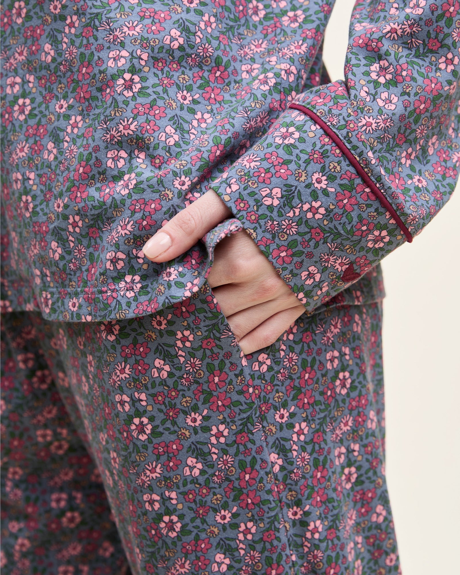 The Women's Pima Pajama Set in Fleurs de Saison features long sleeves and a small floral print in pink, white, and blue on gray. The set includes a button-up top with a chest pocket and matching pants.