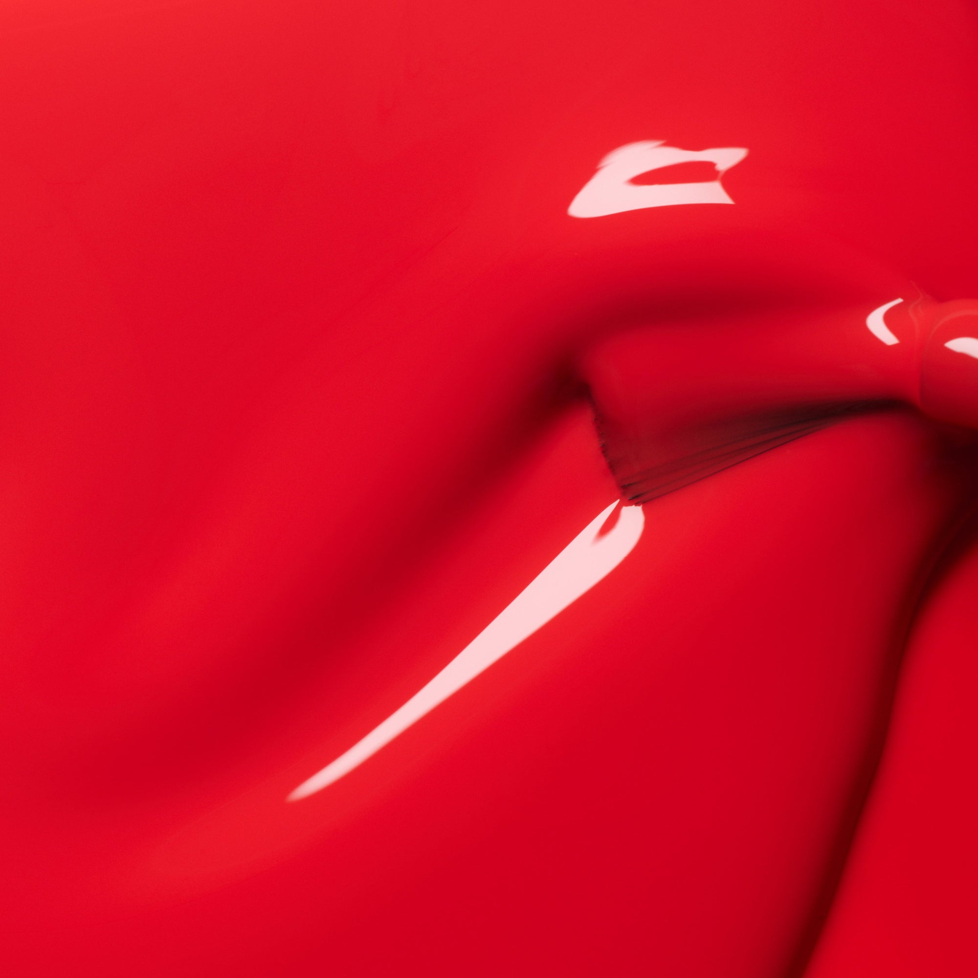 A close-up of glossy red paint with a smooth texture, featuring a shiny, reflective surface and a subtle swirl or indentation near the center.
