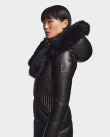 A person stands in profile against a white background, wearing the SHAUNA X - 8121568 BLACK women’s winter coat by Rudsak, featuring black quilting and a large fur-trimmed hood.