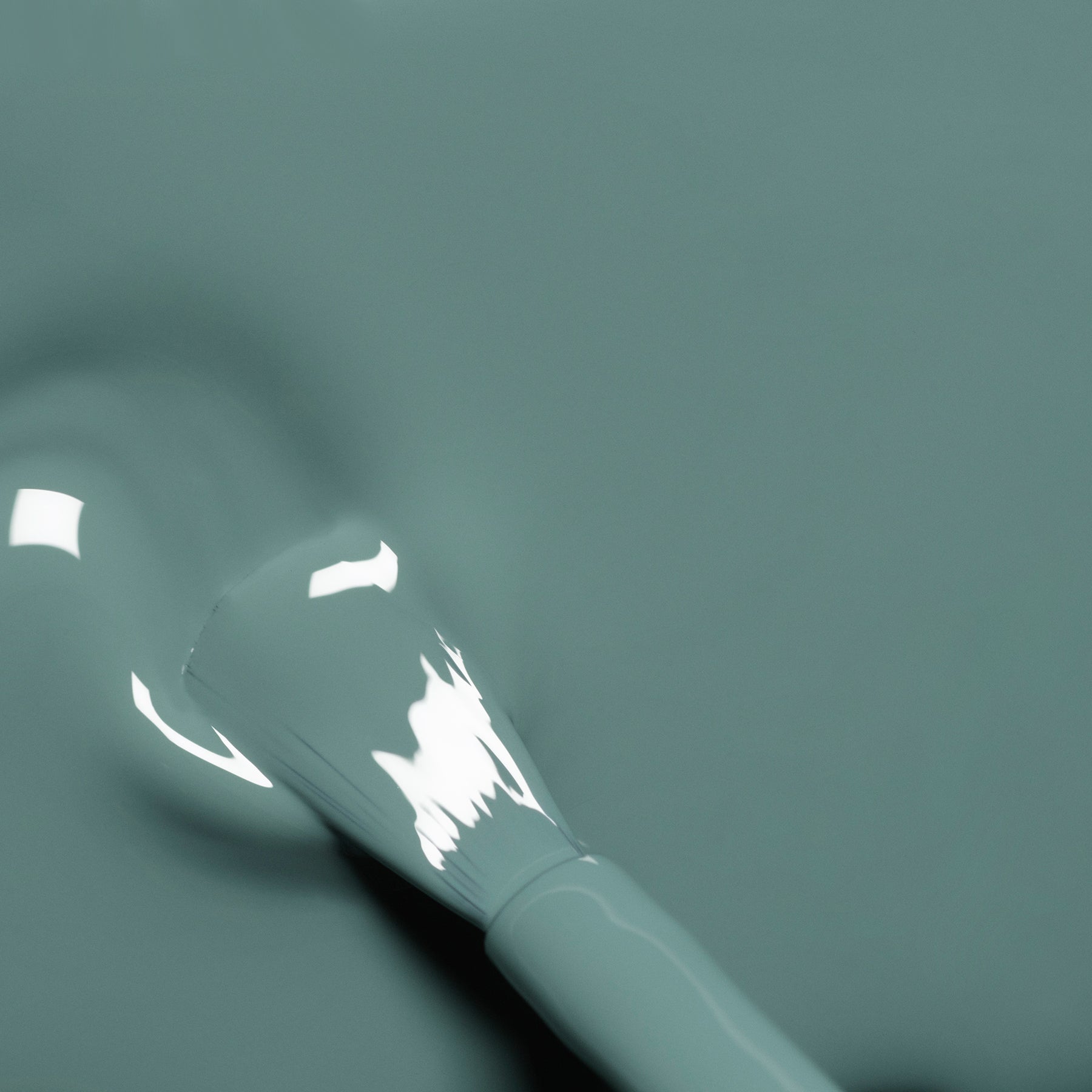 A close-up of a brush applying glossy teal nail polish on a smooth surface, with light reflections visible on the wet polish.