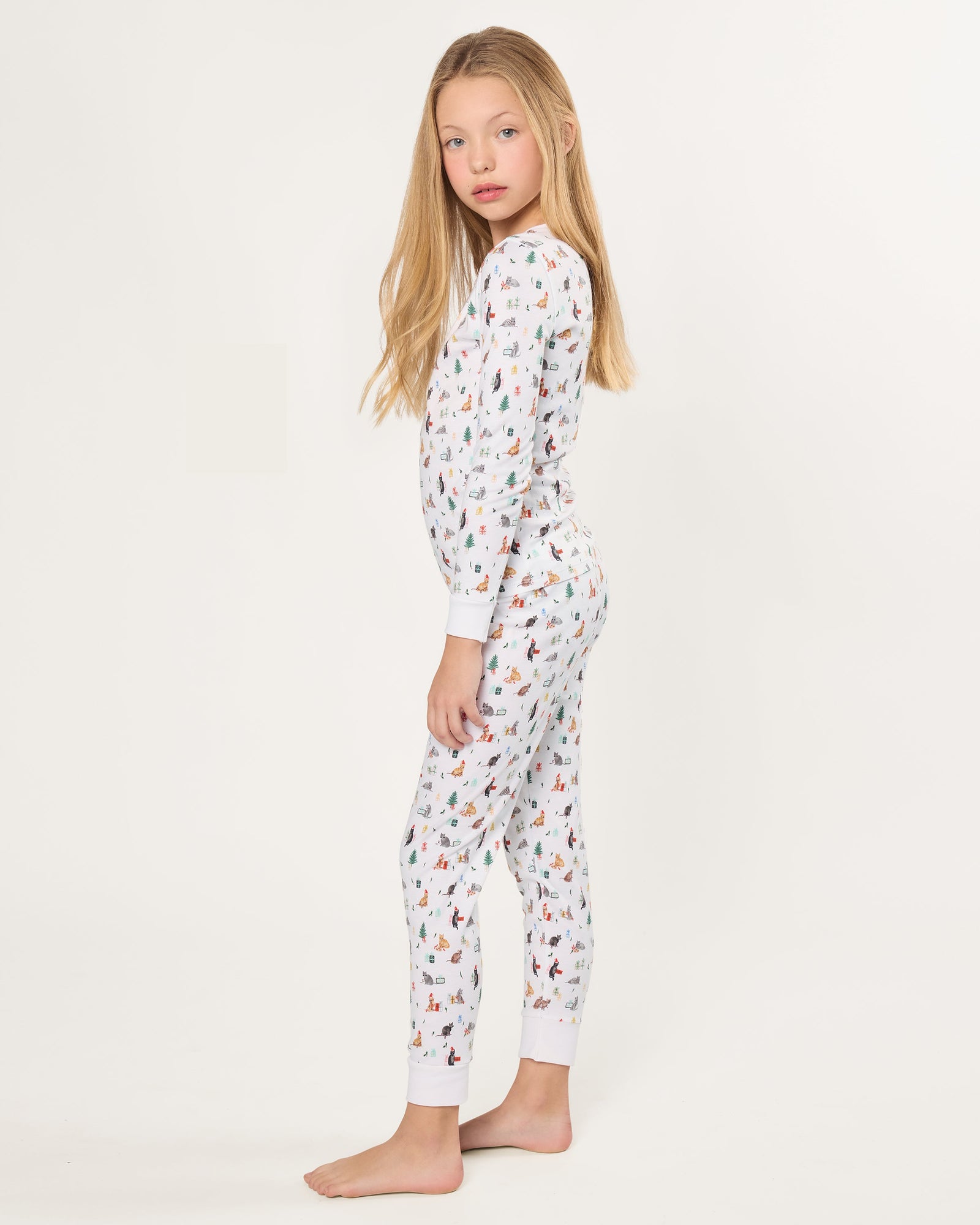 Kid's Pima Snug Fit Pajama Set in Merry Meow features a long-sleeve button-up top and matching pants with winter and holiday-themed prints of cats, trees, presents, and snowmen on a white background.