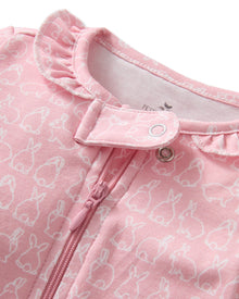 The Baby's Pima Romper in Hoppy Days Pink features long sleeves, white cuffs, a front zipper, a soft white bunny pattern, and a ruffled neckline.