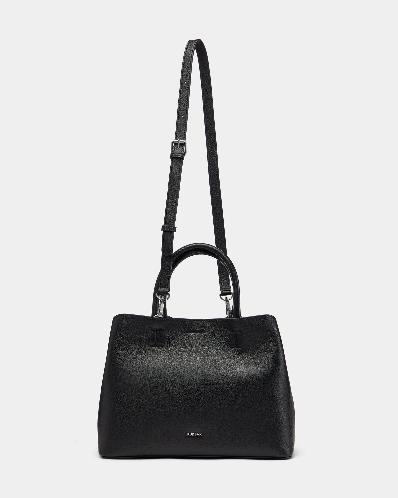 The Rudsak CATIRA S - 8325006 Black is a women’s black pebble leather tote with two short handles, a removable long shoulder strap, minimalist design, and a small silver brand logo on the front.