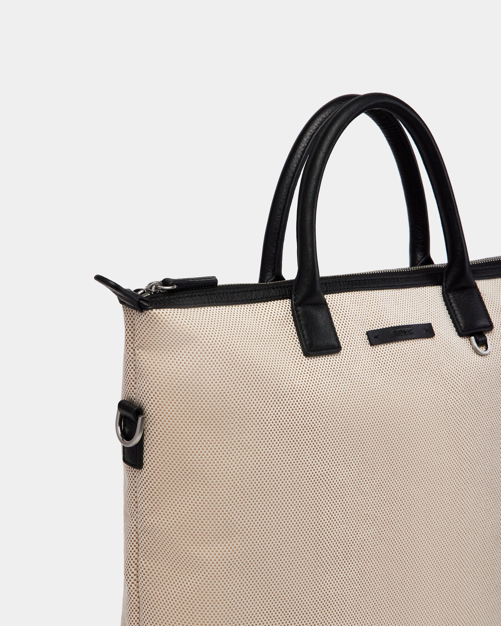 The Rudsak DEXTER - 9324513 Vanilla is a beige textured canvas tote with black leather handles and trim, silver zipper, and metal D-rings—an effortlessly versatile accessory shown against a plain white background.