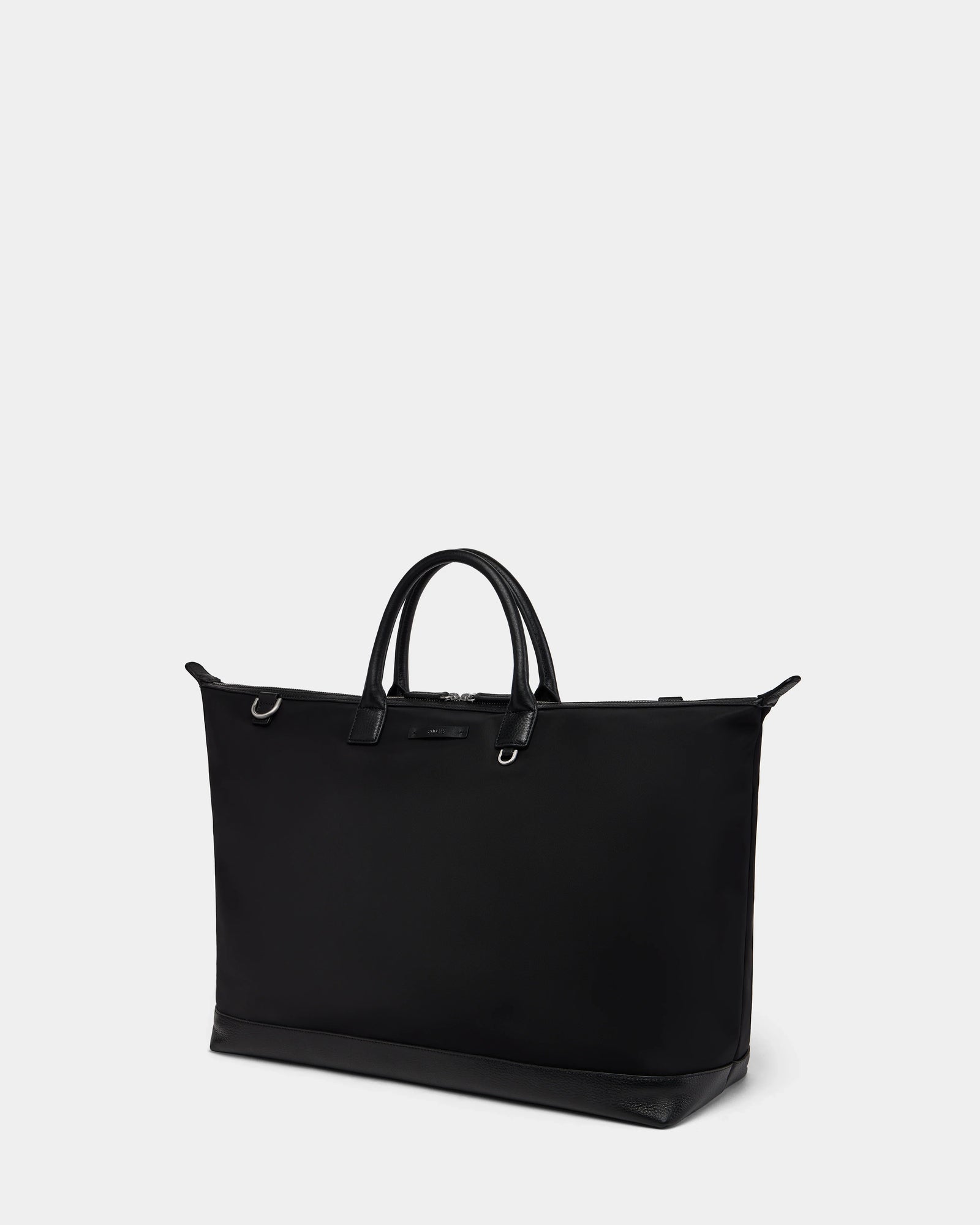 The DUBLIN - 9324514 Black by Rudsak is a sleek, black weekender tote with two short handles, silver-tone hardware, and a structured rectangular shape, shown against a plain light gray background.