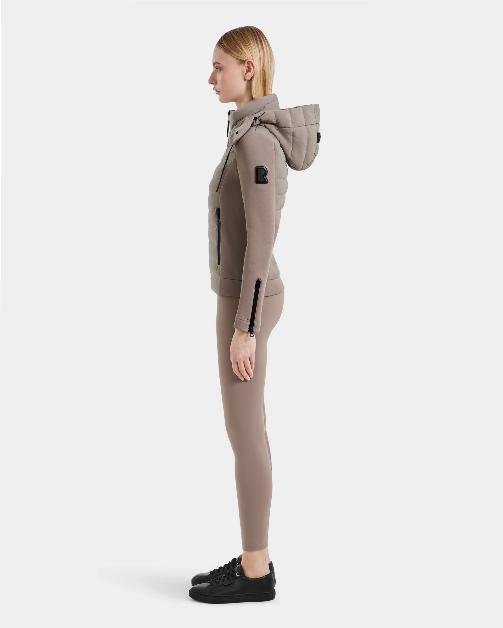 A woman stands in profile wearing the Rudsak MABS - 8124825 Cement fitted jacket with matching leggings and black sneakers, set against a plain white background.