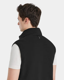 A person with short brown hair, seen from behind, wears a white short-sleeve shirt and the Rudsak MERLO - 6124017 Black men’s vest with a standing collar, its modern quilted style highlighted against a plain light background.