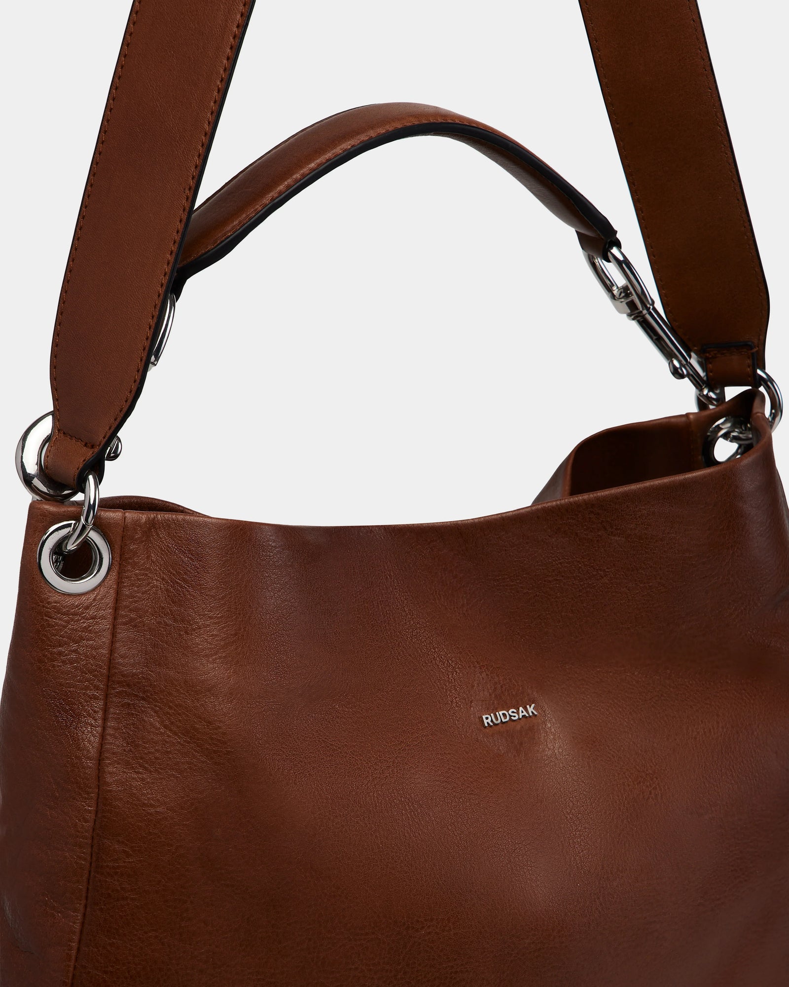 The VIKA - 8325036 Mocha by Rudsak is a brown leather shoulder bag with silver hardware, a wide strap, and a subtle front logo—an ideal stylish everyday womens accessory shown against a light background.
