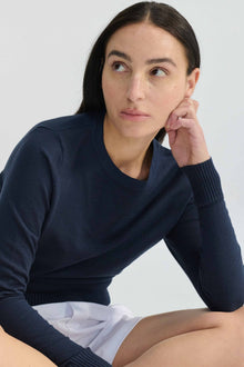 Woman wearing a navy blue sweater and white shorts against a light background