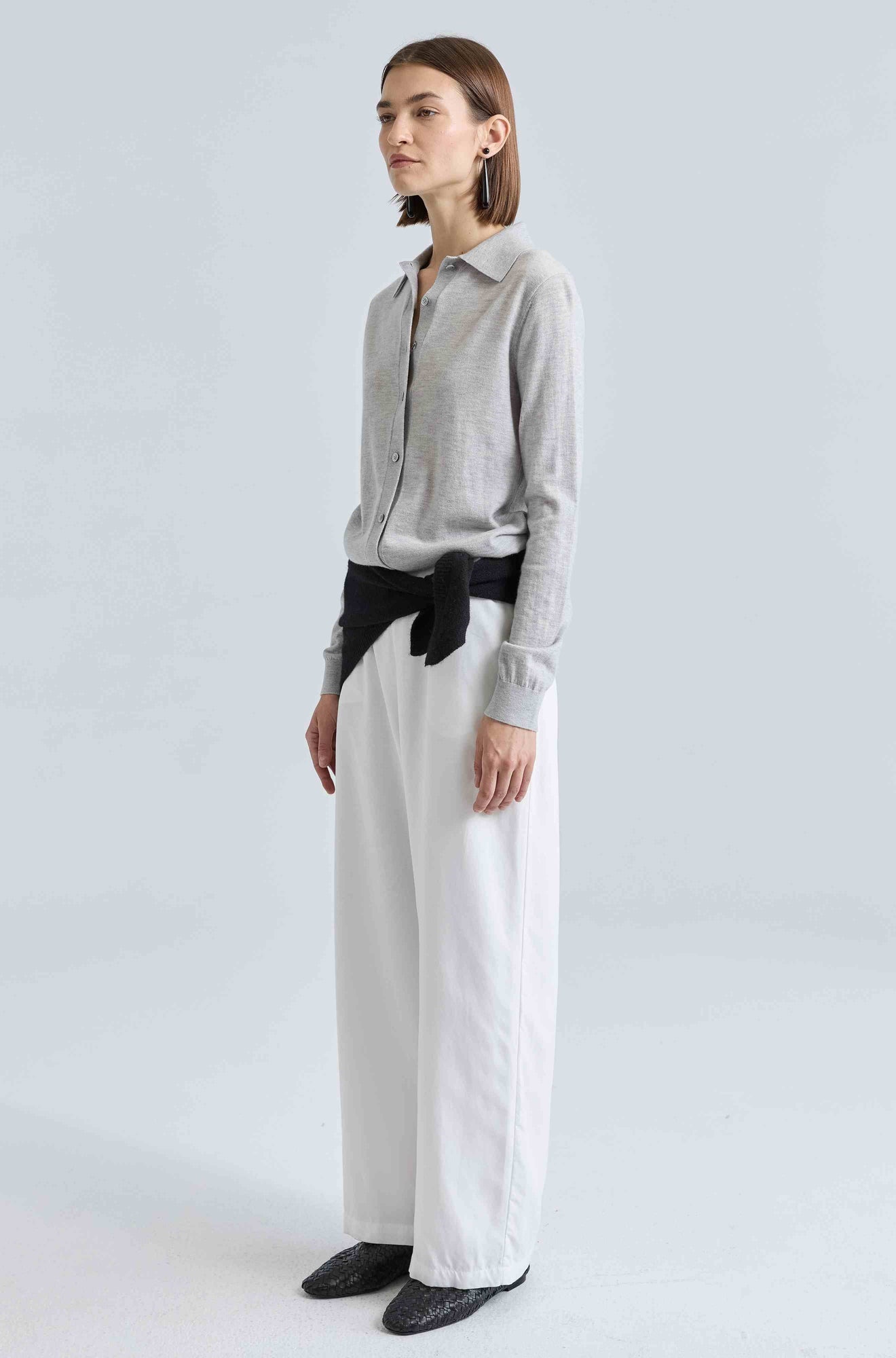 Woman wearing a gray shirt and white pants against a light gray background