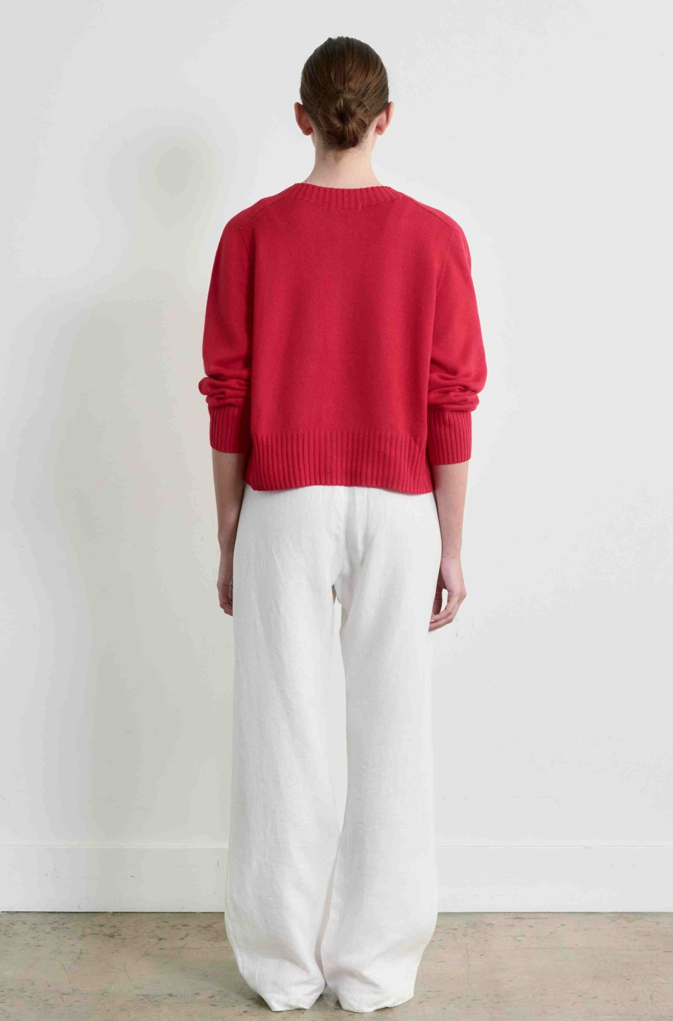 Person wearing a red sweater and white pants standing against a plain background